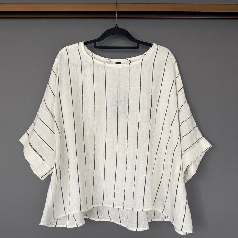 A white short-sleeve blouse with thin vertical black stripes, hanging on a black hanger against a dark gray wall.